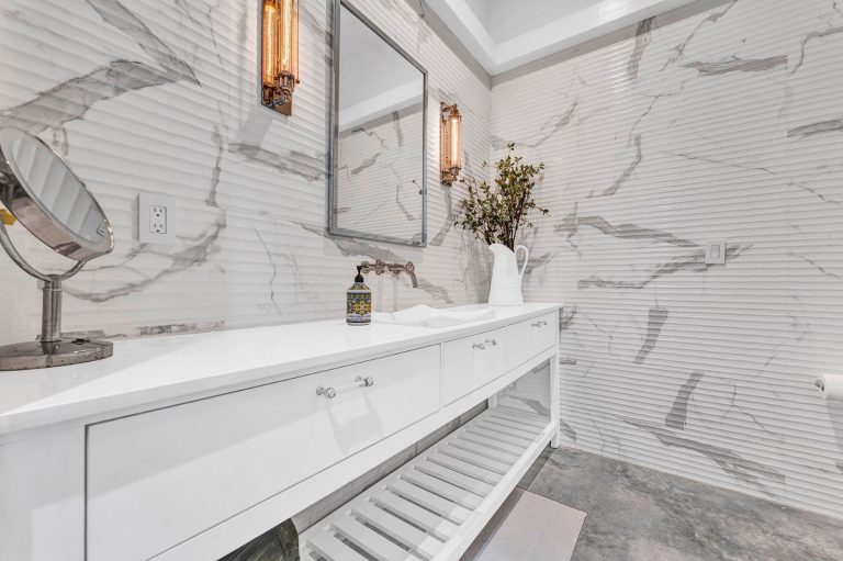 Long white bathroom vanity surrounded by marble-patterned finishes